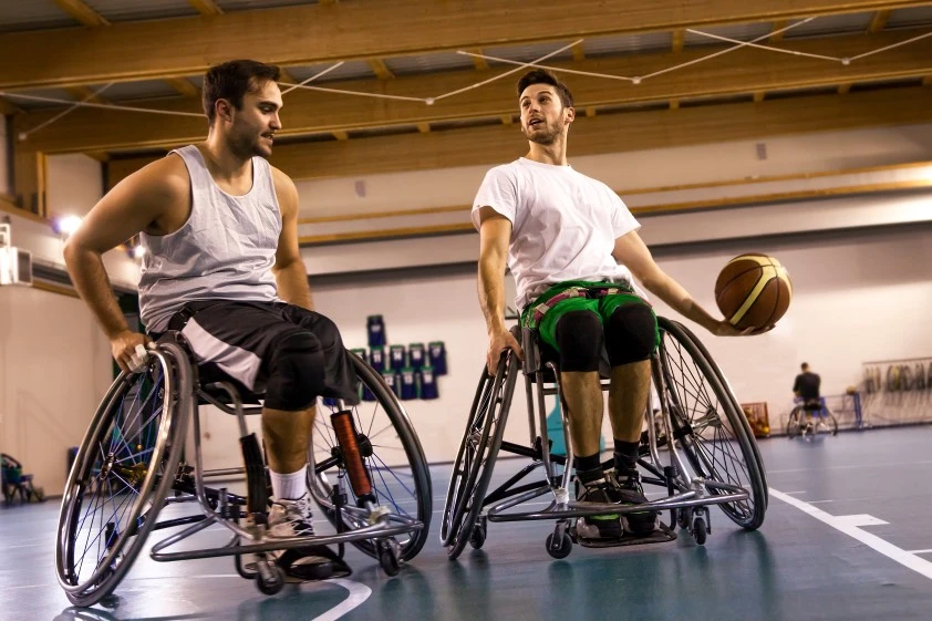 Two disabled men sitting on their wheelchairs playing indoor basketball