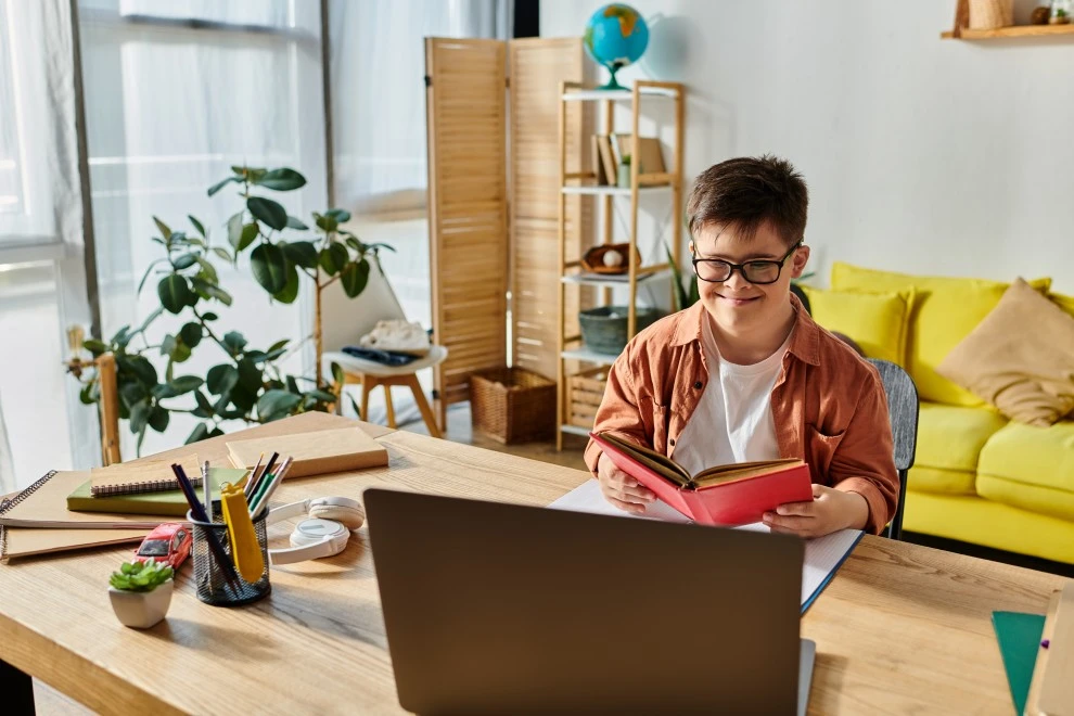 Disabled man holding a book while smiling and looking at his laptop