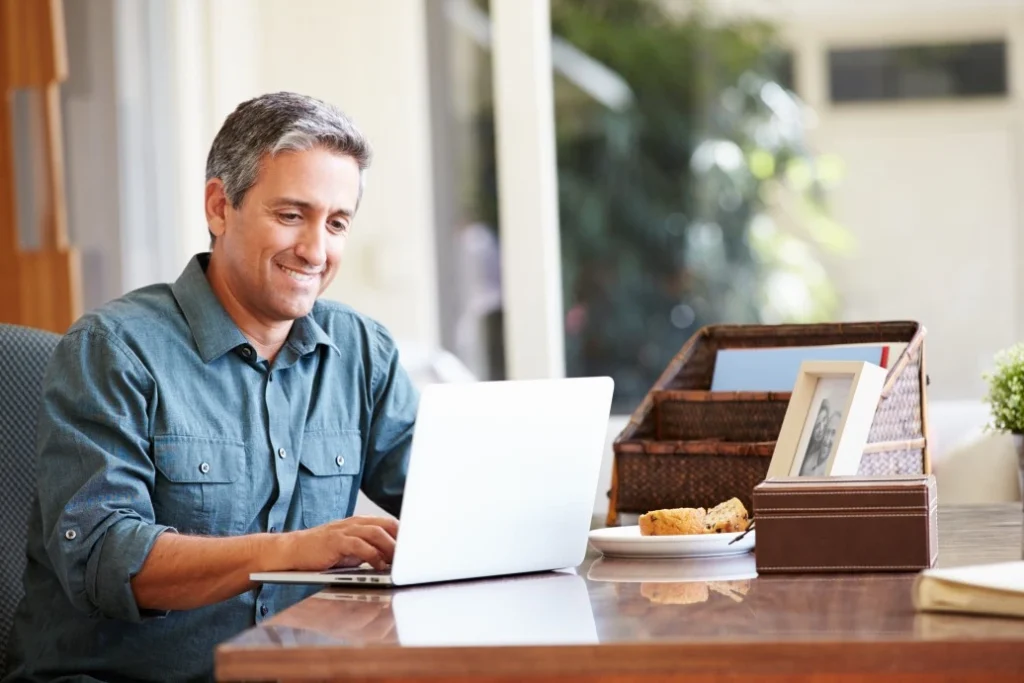 A man smiling while typing on his laptop